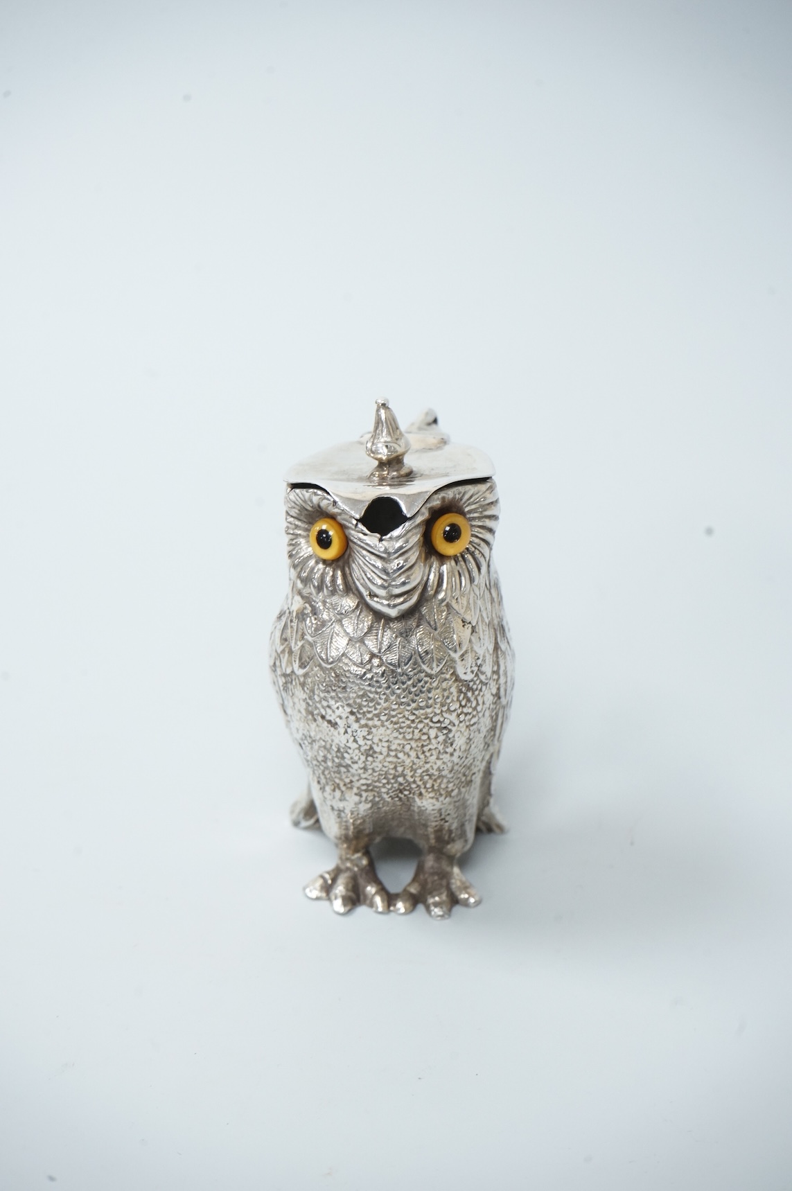 A novelty white metal single handled mustard pot, modelled as a free-standing owl, with hinged cover and textured 'feathers', unmarked, height 95mm.